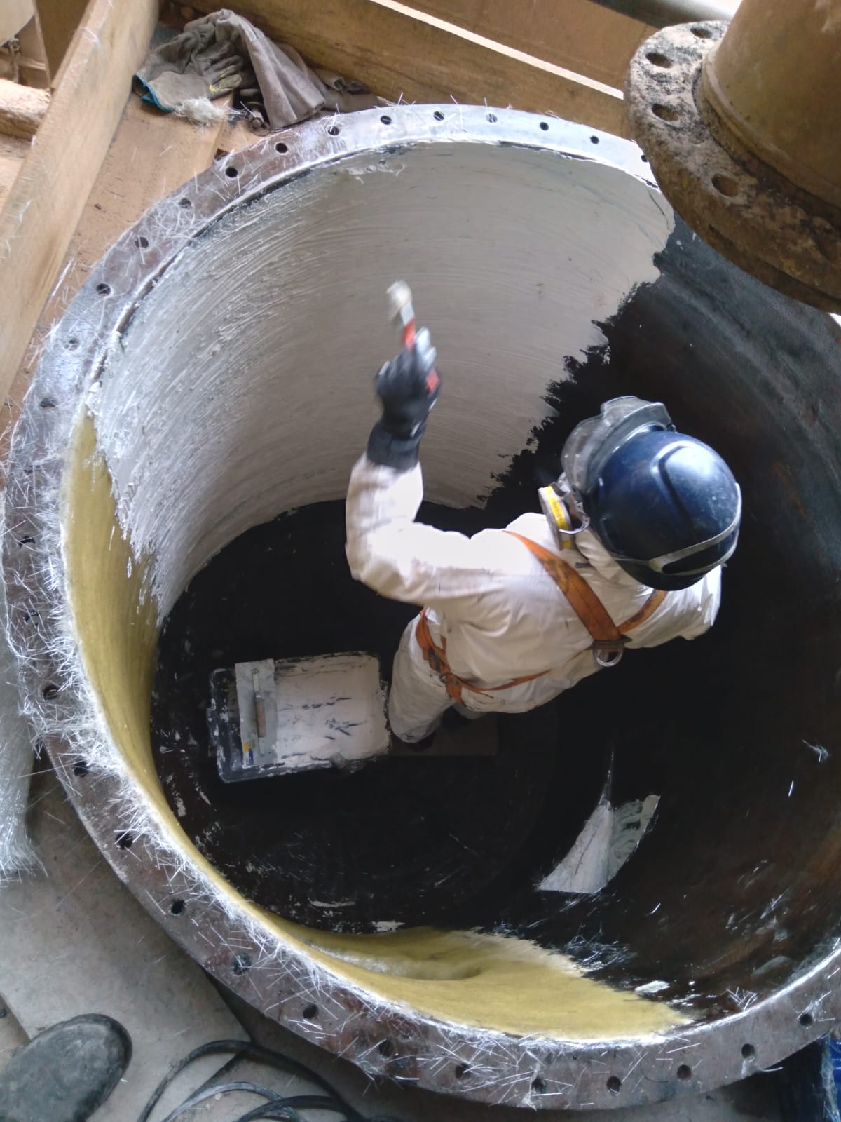 Técnico aplicando revestimento interno em tanque flangeado de grande diâmetro