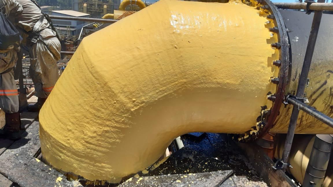 Curva de 90 graus de grande diâmetro recém-laminada em amarelo, junto ao flange, com técnico ao lado