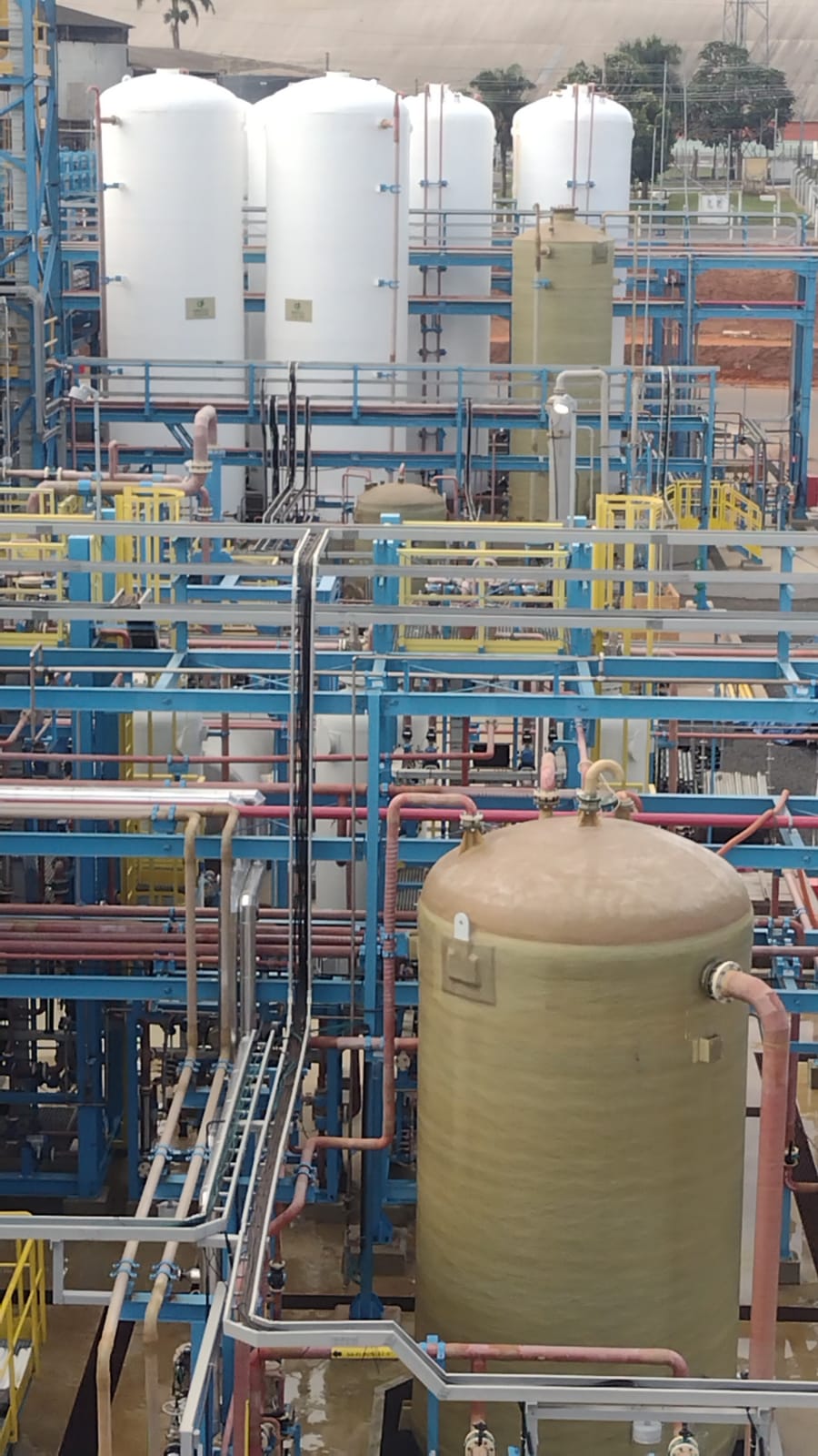 Vista geral de planta industrial com tanques verticais, rede de tubulação e vaso em PRFV